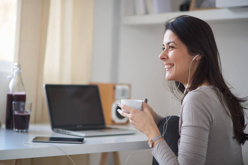 Frau arbeitet lachend am Tablet zu Hause und hält eine Tasse Kaffee