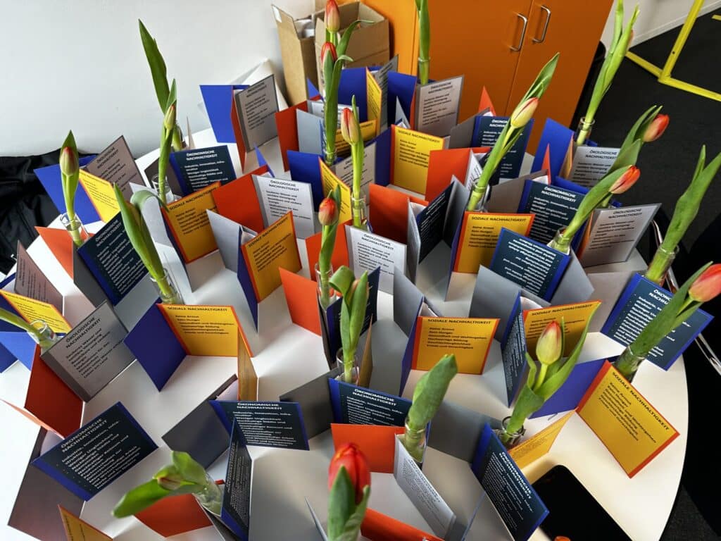 Offene Informationskarten zum Thema Nachhaltigkeit sind auf einem Tisch aufgestellt. Dazwischen stehen Tulpen.